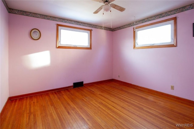 empty room with light wood-style floors, a wealth of natural light, visible vents, and baseboards