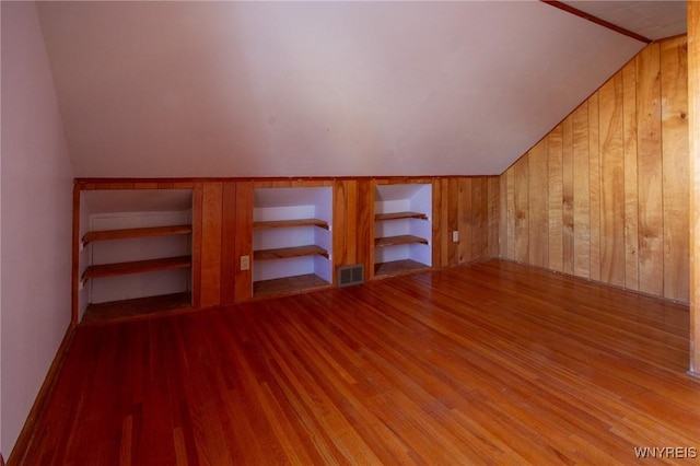 additional living space featuring visible vents, vaulted ceiling, wooden walls, and wood finished floors