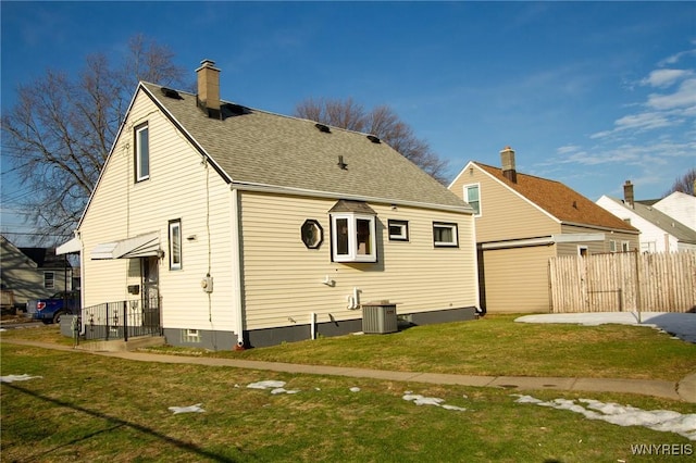 back of property with roof with shingles, a chimney, central air condition unit, a lawn, and fence