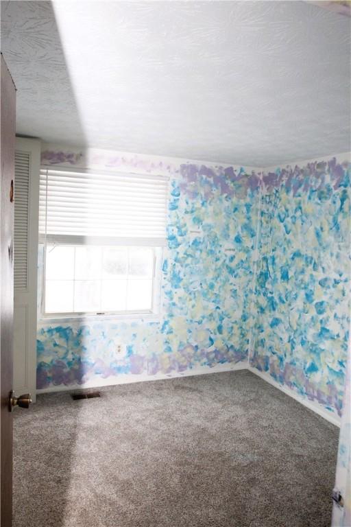 empty room featuring carpet, visible vents, and wallpapered walls