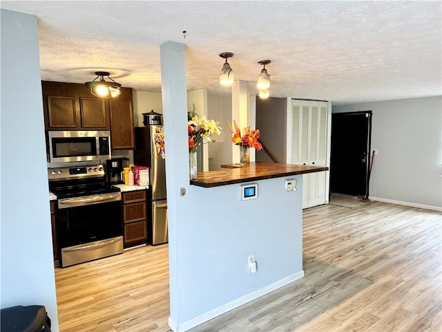 kitchen with baseboards, butcher block counters, light wood-style flooring, stainless steel appliances, and a textured ceiling