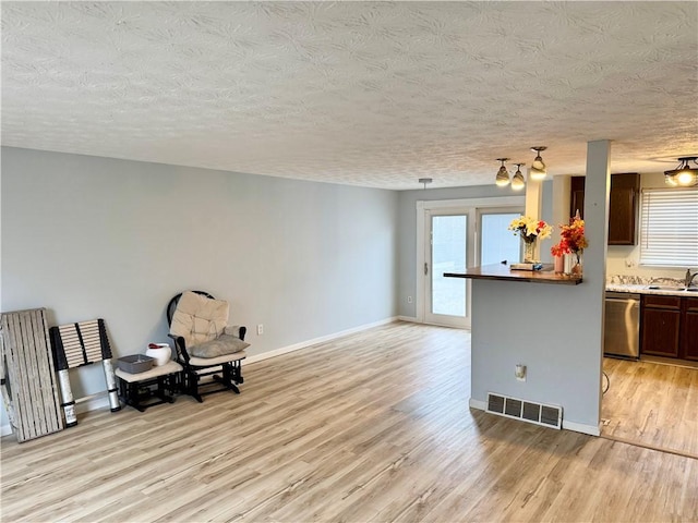 living area with a textured ceiling, light wood finished floors, visible vents, and baseboards