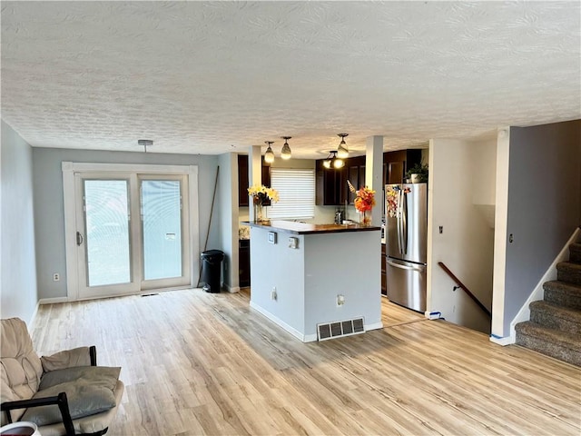 kitchen featuring a textured ceiling, visible vents, light wood-style floors, open floor plan, and freestanding refrigerator