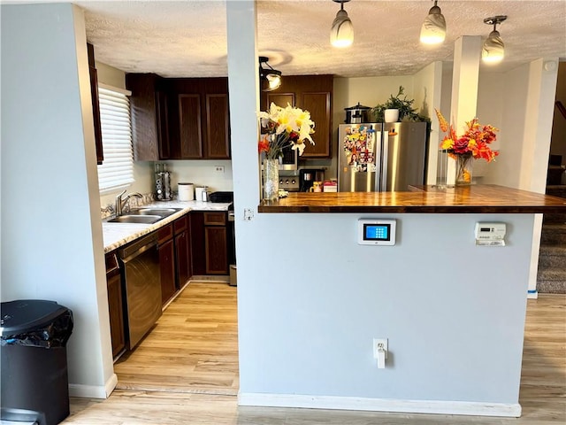 kitchen featuring dark brown cabinetry, butcher block counters, light wood-style flooring, appliances with stainless steel finishes, and a sink