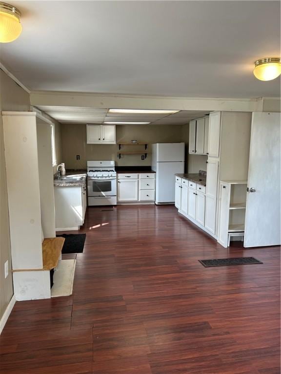 kitchen featuring dark wood finished floors, dark countertops, white cabinets, a sink, and white appliances