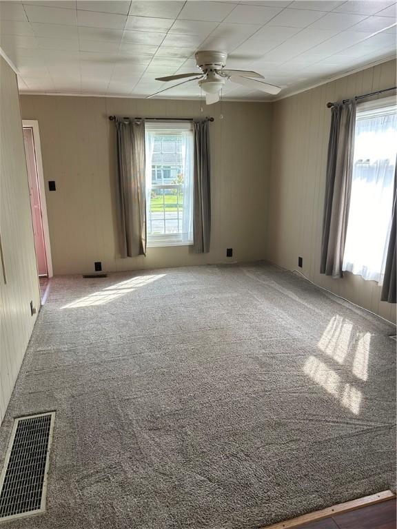 carpeted empty room with a healthy amount of sunlight, visible vents, and a ceiling fan