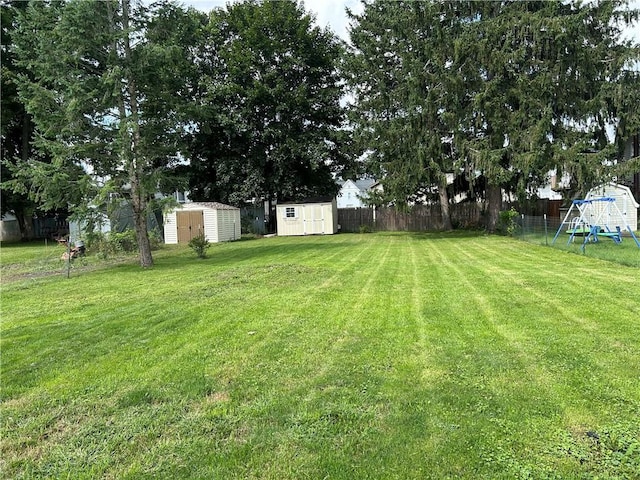 view of yard featuring a storage shed, a playground, fence, and an outbuilding