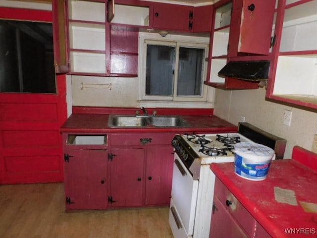 kitchen featuring exhaust hood, a sink, light wood-style floors, gas range gas stove, and dark countertops