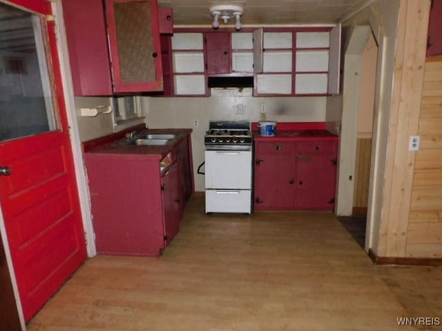 kitchen featuring white gas stove, under cabinet range hood, a sink, red cabinets, and dark countertops