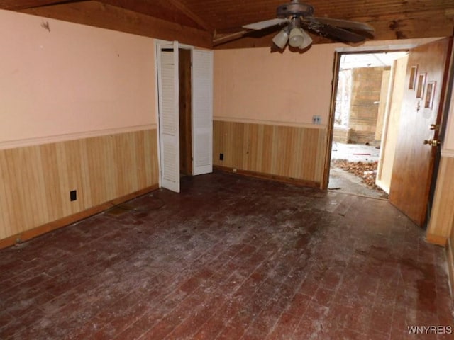 unfurnished room featuring lofted ceiling, wood walls, a ceiling fan, and wainscoting