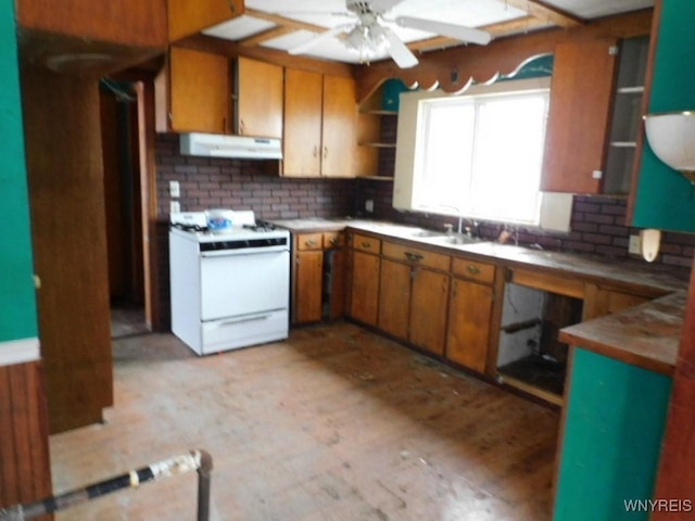 kitchen with under cabinet range hood, a sink, brown cabinets, open shelves, and white gas range