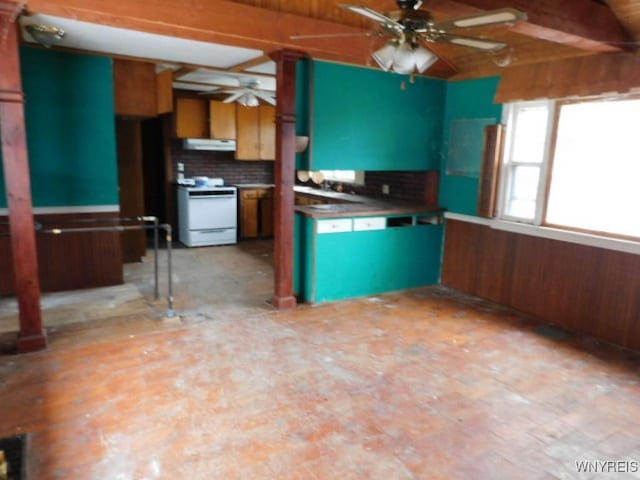 kitchen featuring tasteful backsplash, wooden walls, ceiling fan, stove, and under cabinet range hood