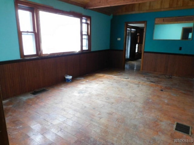 unfurnished room featuring a wainscoted wall, visible vents, and wooden walls