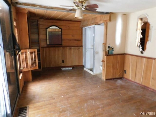 unfurnished room featuring wooden walls, visible vents, a ceiling fan, wainscoting, and wood finished floors