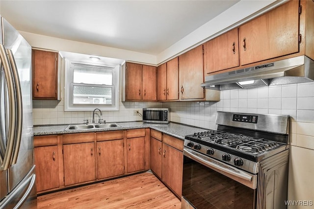 kitchen featuring brown cabinets, light wood-style flooring, appliances with stainless steel finishes, a sink, and under cabinet range hood