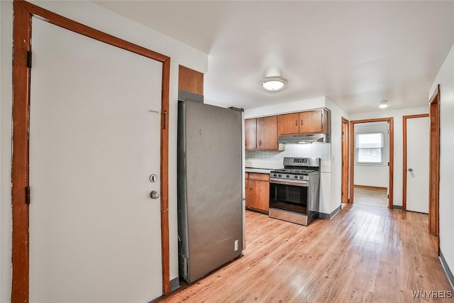 kitchen featuring brown cabinetry, stainless steel appliances, light wood-type flooring, under cabinet range hood, and backsplash