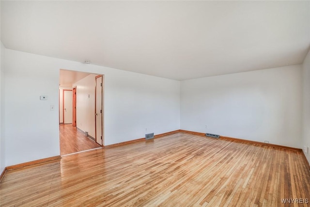 empty room with light wood finished floors, visible vents, and baseboards