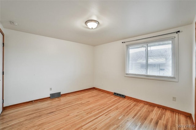 spare room featuring baseboards, visible vents, and wood finished floors