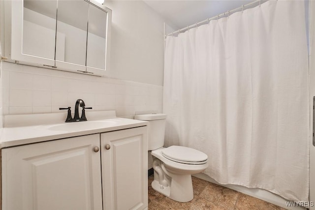 full bathroom featuring toilet, stone finish floor, curtained shower, vanity, and tile walls