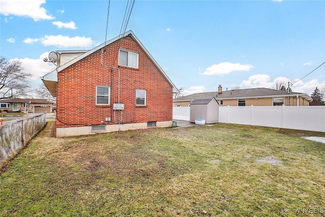 back of house with a yard, a fenced backyard, an outbuilding, and brick siding