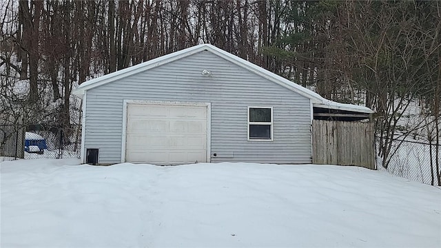 snow covered garage featuring a garage and fence