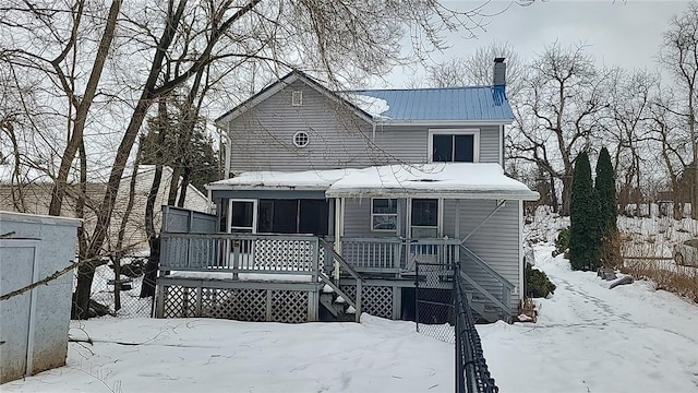 snow covered house with stairs, metal roof, a deck, and fence