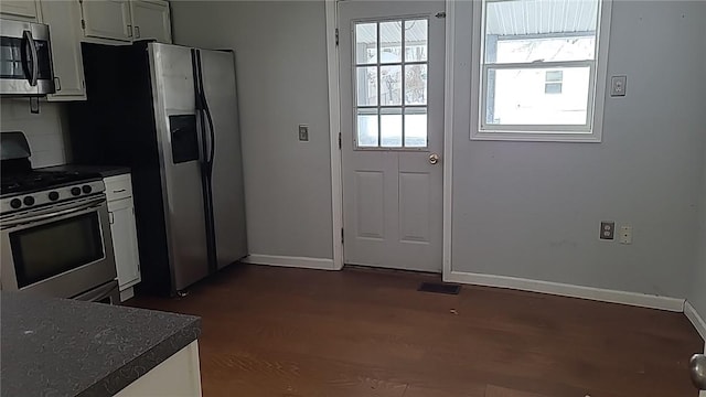 kitchen with baseboards, decorative backsplash, dark countertops, dark wood-type flooring, and stainless steel appliances