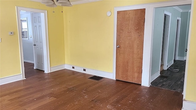 spare room featuring baseboards, wood finished floors, visible vents, and crown molding