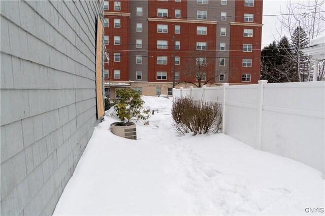 snowy yard featuring central AC unit and fence