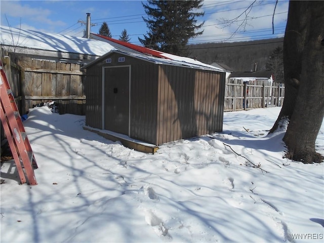 snow covered structure featuring a shed, fence, and an outbuilding