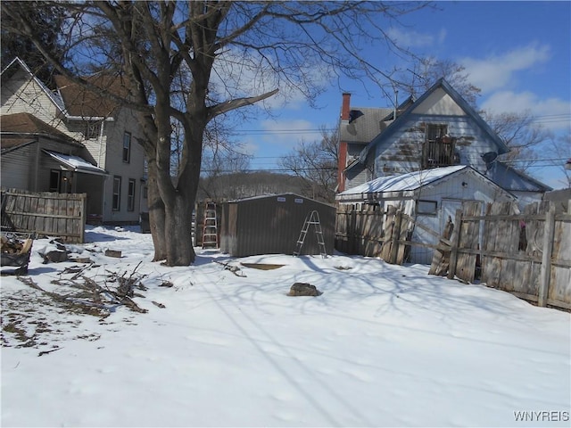 yard covered in snow with a shed, fence, and an outdoor structure