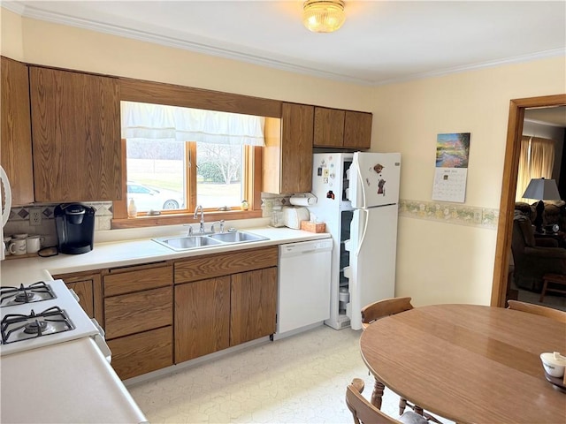 kitchen featuring white appliances, brown cabinets, light countertops, crown molding, and a sink