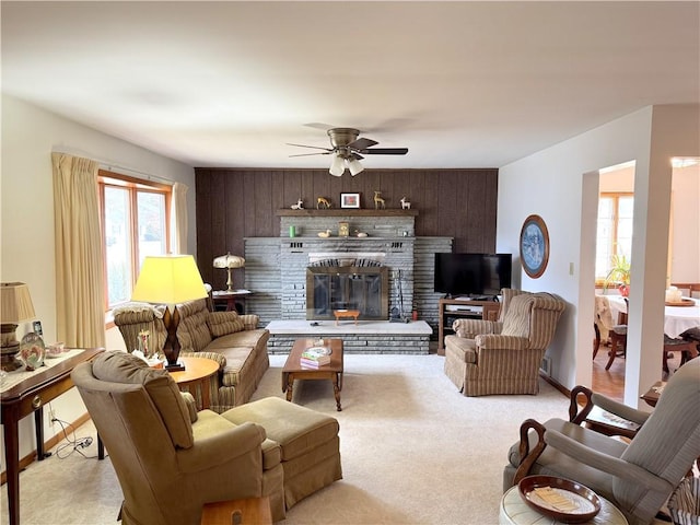 carpeted living room with wood walls, a glass covered fireplace, a ceiling fan, and baseboards