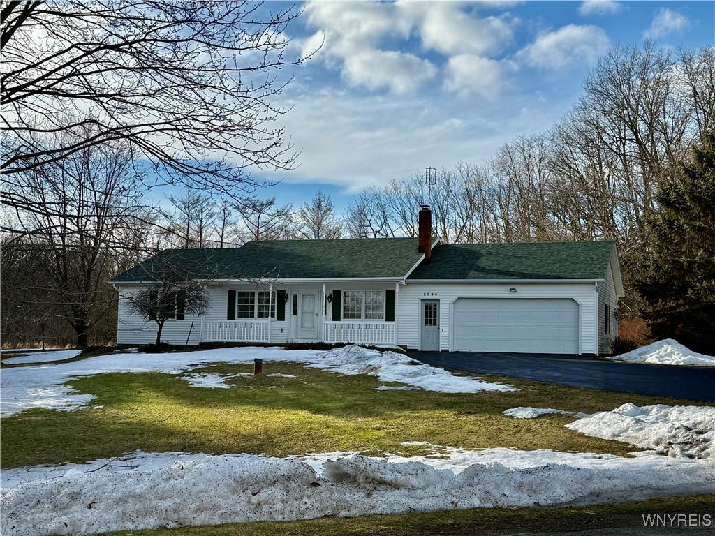 view of front of property featuring aphalt driveway, a chimney, covered porch, a lawn, and a garage