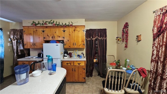 kitchen with light tile patterned floors, brown cabinetry, light countertops, and freestanding refrigerator