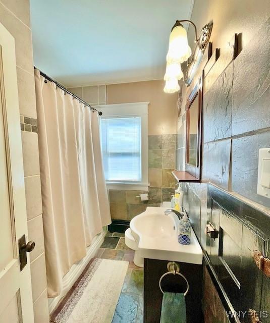 full bathroom featuring a shower with curtain, tile walls, stone tile floors, and vanity