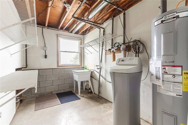 clothes washing area with concrete block wall, laundry area, and electric water heater