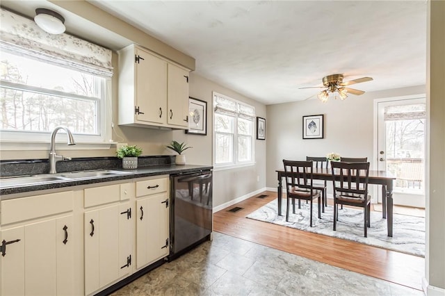 kitchen with a sink, a ceiling fan, baseboards, black dishwasher, and dark countertops