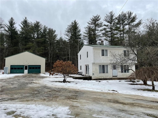 view of snow covered exterior with a detached garage, a chimney, and an outdoor structure