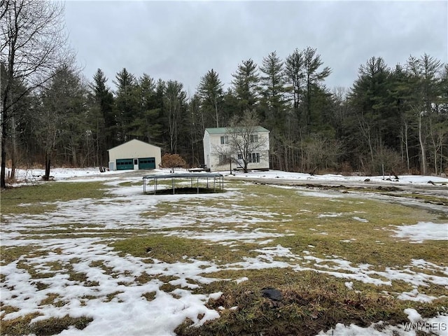 yard covered in snow with an outdoor structure, a view of trees, and a detached garage