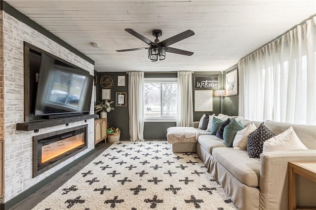 living area featuring a glass covered fireplace, ceiling fan, and wood finished floors