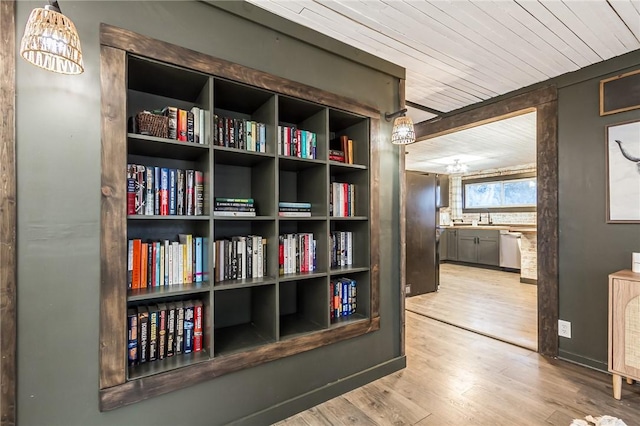 hallway featuring wooden ceiling, a sink, baseboards, and wood finished floors