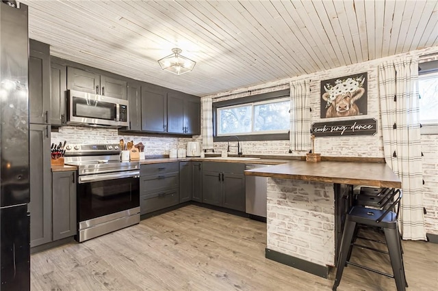 kitchen featuring appliances with stainless steel finishes, light wood-type flooring, a sink, and a kitchen breakfast bar