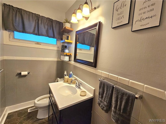 bathroom featuring toilet, a wainscoted wall, vanity, visible vents, and tile walls