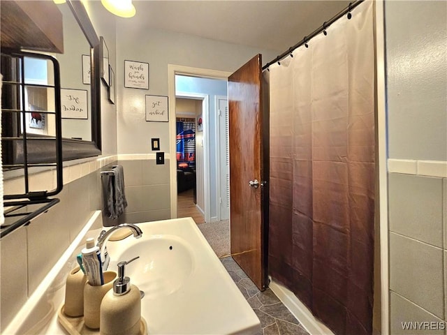 bathroom featuring wainscoting, a shower with shower curtain, a sink, and tile walls