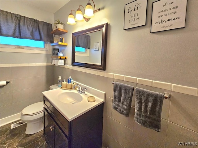 bathroom featuring a wainscoted wall, tile walls, visible vents, toilet, and vanity