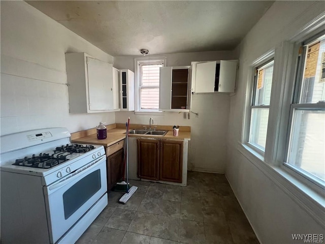 kitchen with white cabinets, light countertops, a sink, and white gas stove