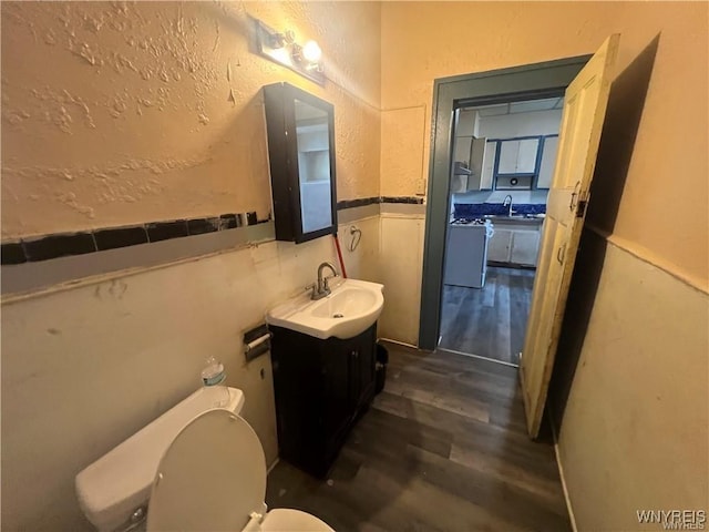 bathroom featuring a textured wall, toilet, a wainscoted wall, wood finished floors, and vanity