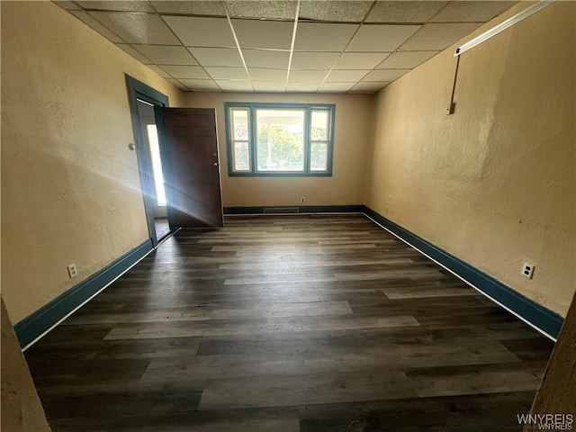 spare room with a textured wall, dark wood-type flooring, a paneled ceiling, and baseboards