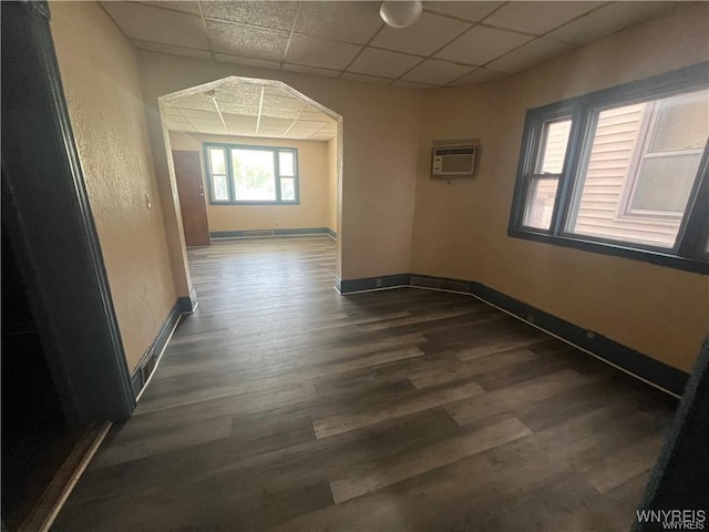 hallway featuring a drop ceiling, a wall mounted air conditioner, dark wood finished floors, and baseboards